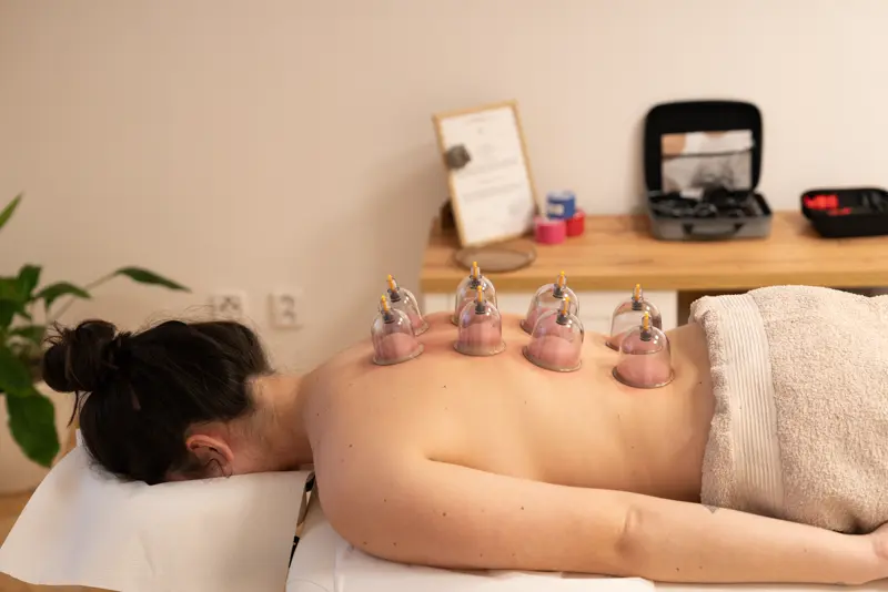 A client resting on a massage table with transparent cupping vessels on the back.