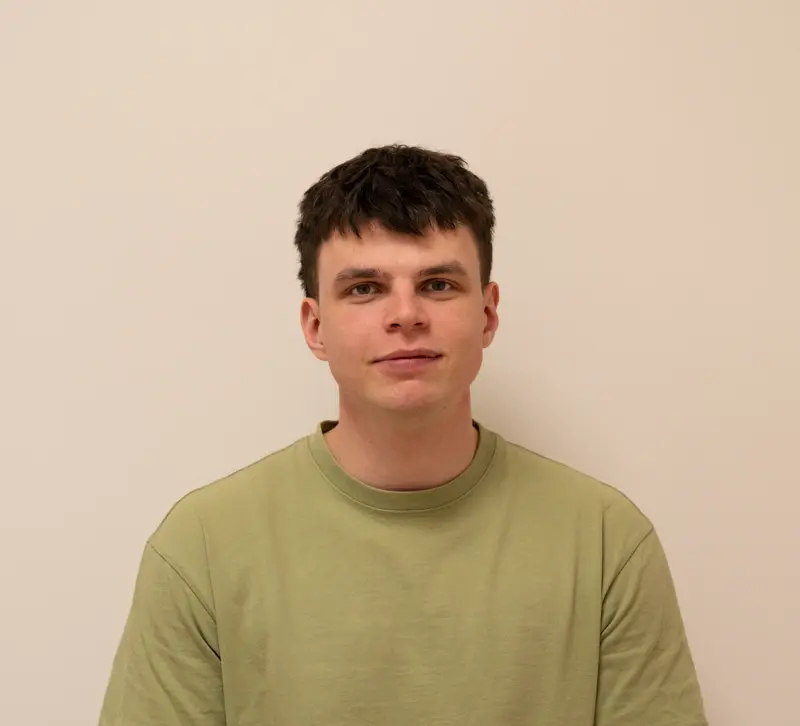 A portrait of the massage therapist in a green T-shirt against a warm neutral background.
