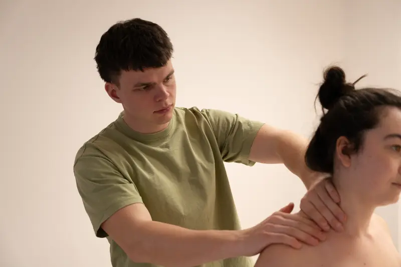 The therapist working on a seated client’s shoulders in the massage studio.
